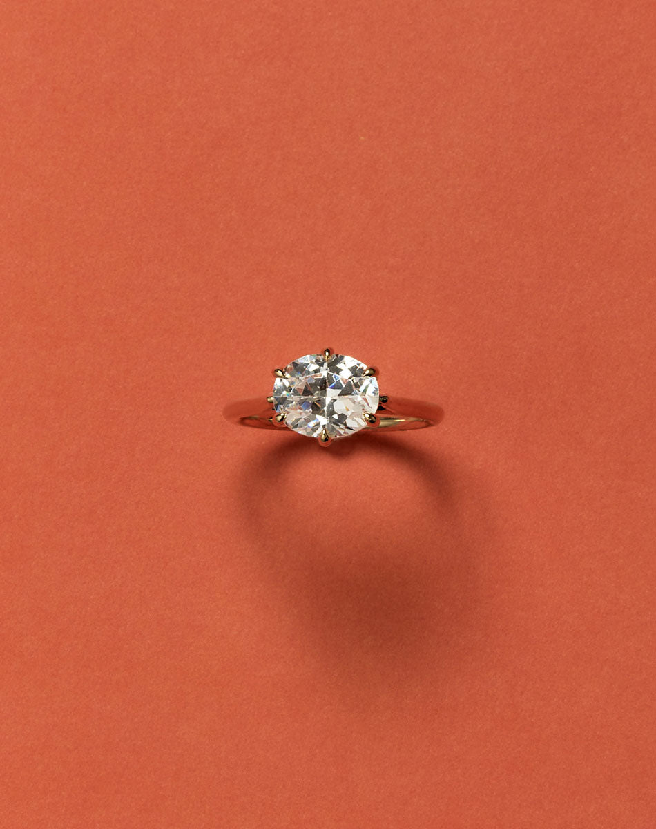 Yellow gold oval east west diamond solitaire engagement ring on orage background.