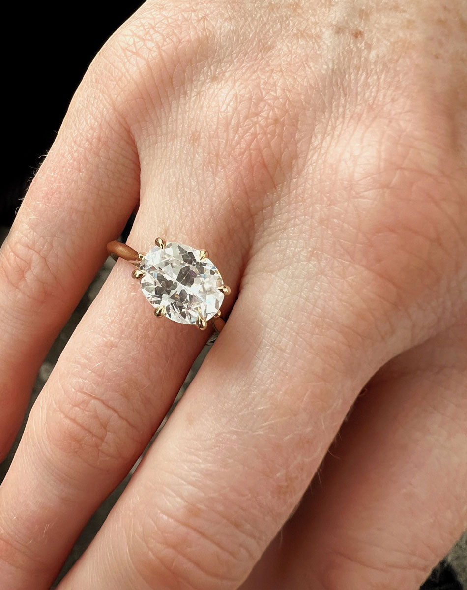 Yellow gold oval east west diamond solitaire engagement ring worn on hand.