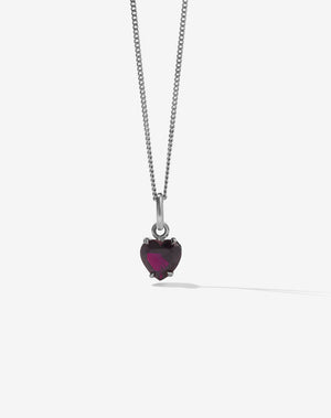 Heart-shaped pendant with a garnet gemstone on a silver chain against a white background