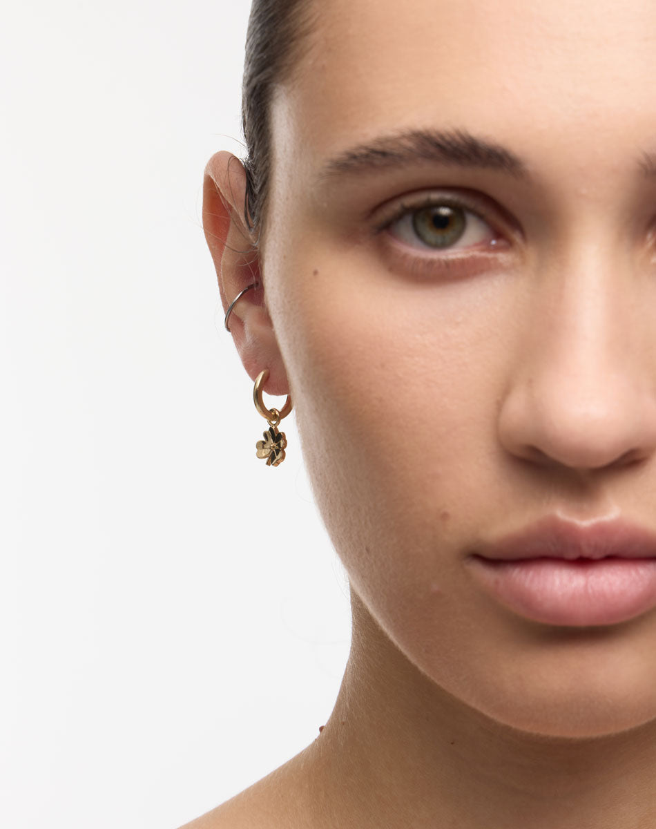 Close-up of a person wearing gold four leaf clover earrings with a plain background