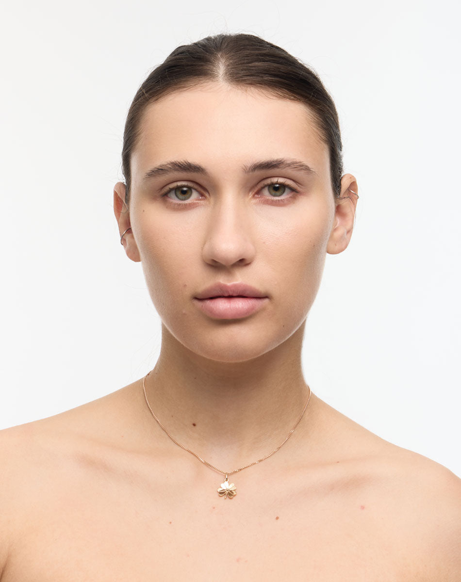 Woman wearing a gold necklace with a lucky four leaf clover pendant on a white background