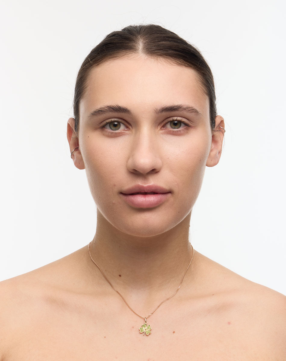 Woman wearing a gold four leaf clover necklace set with green stones on a white background