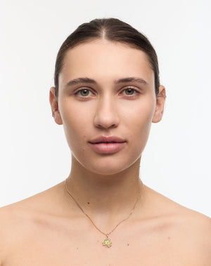 Woman wearing a gold four leaf clover necklace set with green stones on a white background