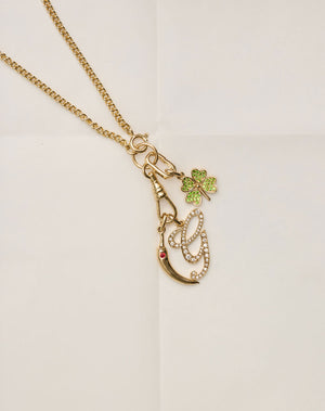 Gold necklace with a pendant featuring a green clover and red gem on a light background