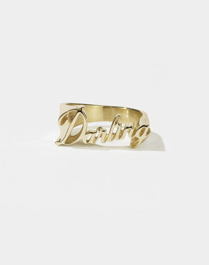 A gold-plated, flat-top knuckle duster style ring with the word 'DARLING' in cursive script.