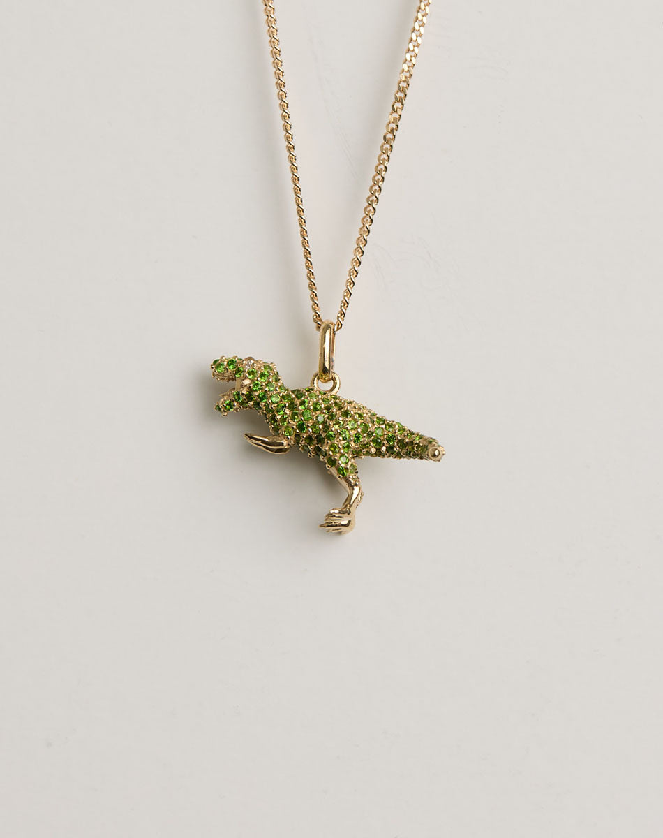 Gold necklace with a green gemstone set dinosaur pendant on a light grey background