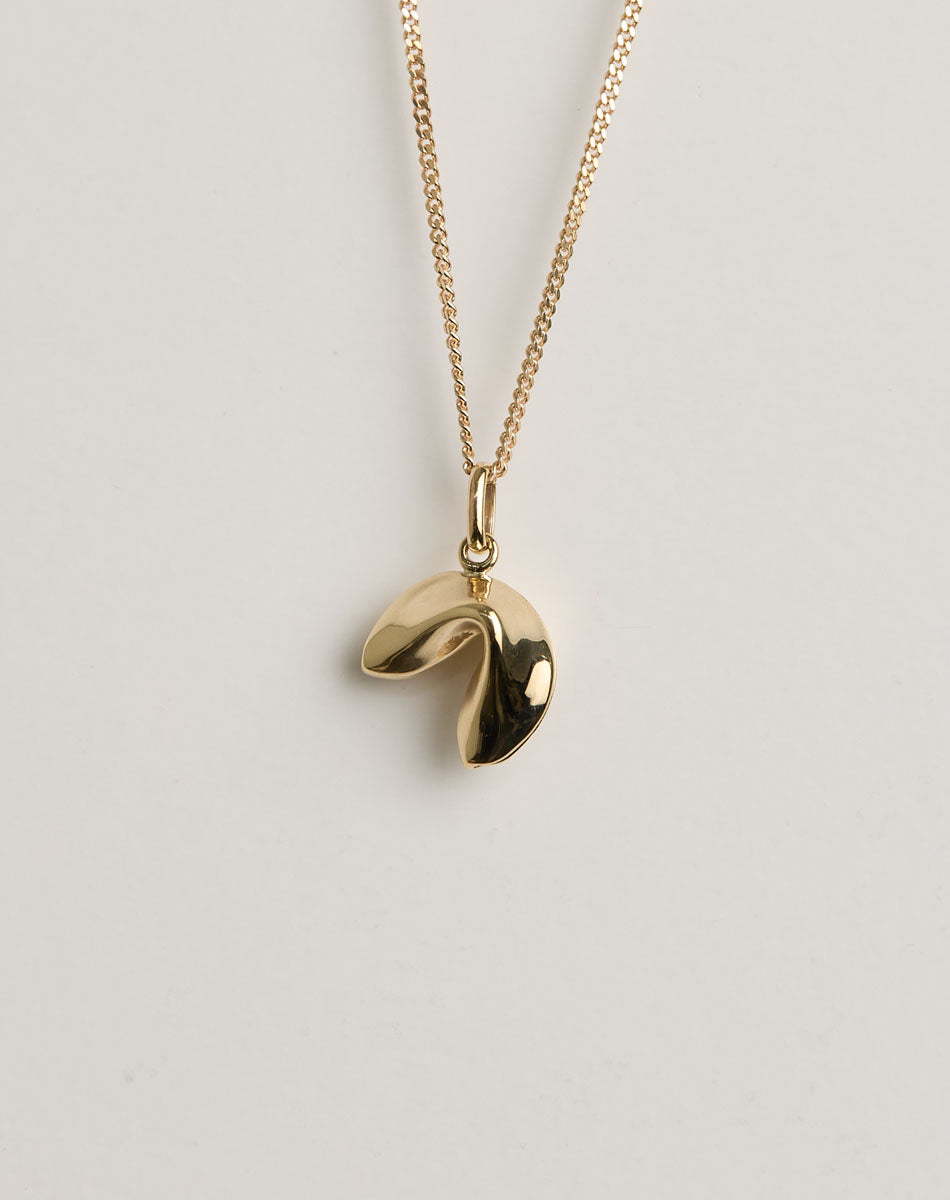 Gold necklace with a lucky fortune cookie pendant on a light grey background