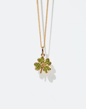 Gold necklace with a four-leaf clover pendant set with green gemstones on a white background