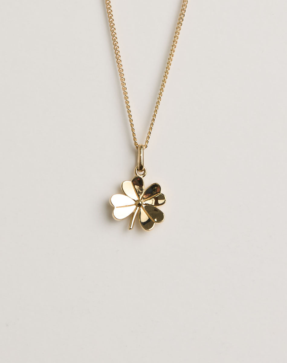 Gold four-leaf clover necklace on a light grey background