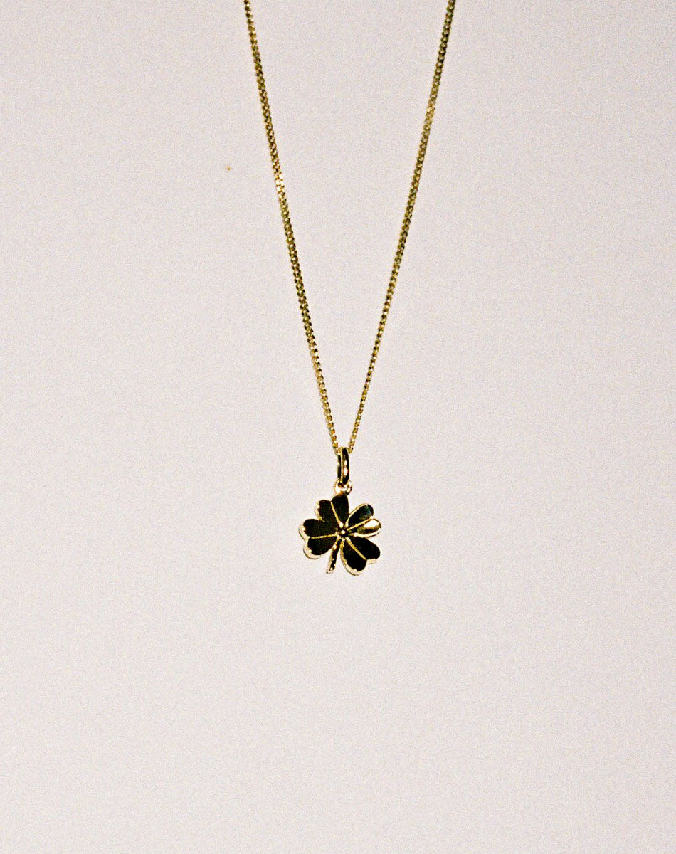Gold necklace with a lucky four leaf clover pendant on a grey background