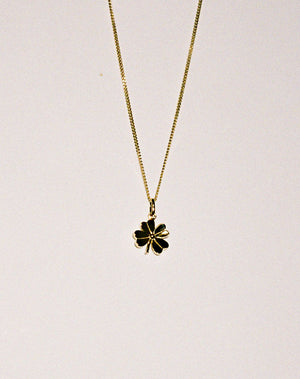 Gold necklace with a lucky four leaf clover pendant on a grey background