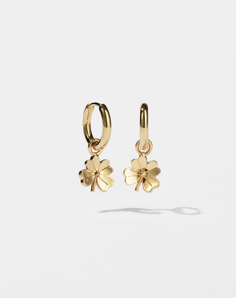 Gold hoop earrings with for leaf clover charms on a light grey background