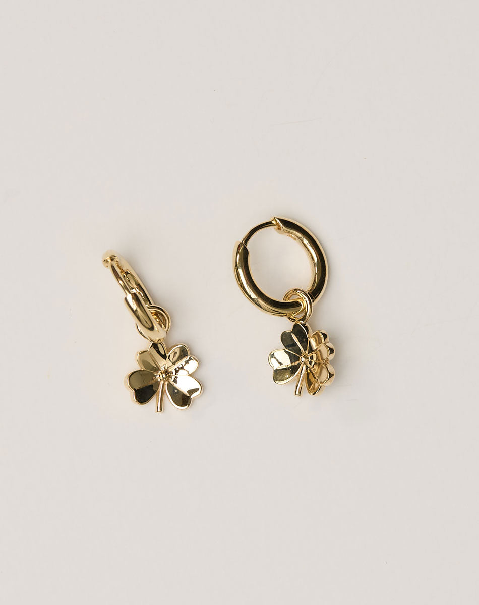 Gold hoop earrings with four-leaf clover charms on a light beige background