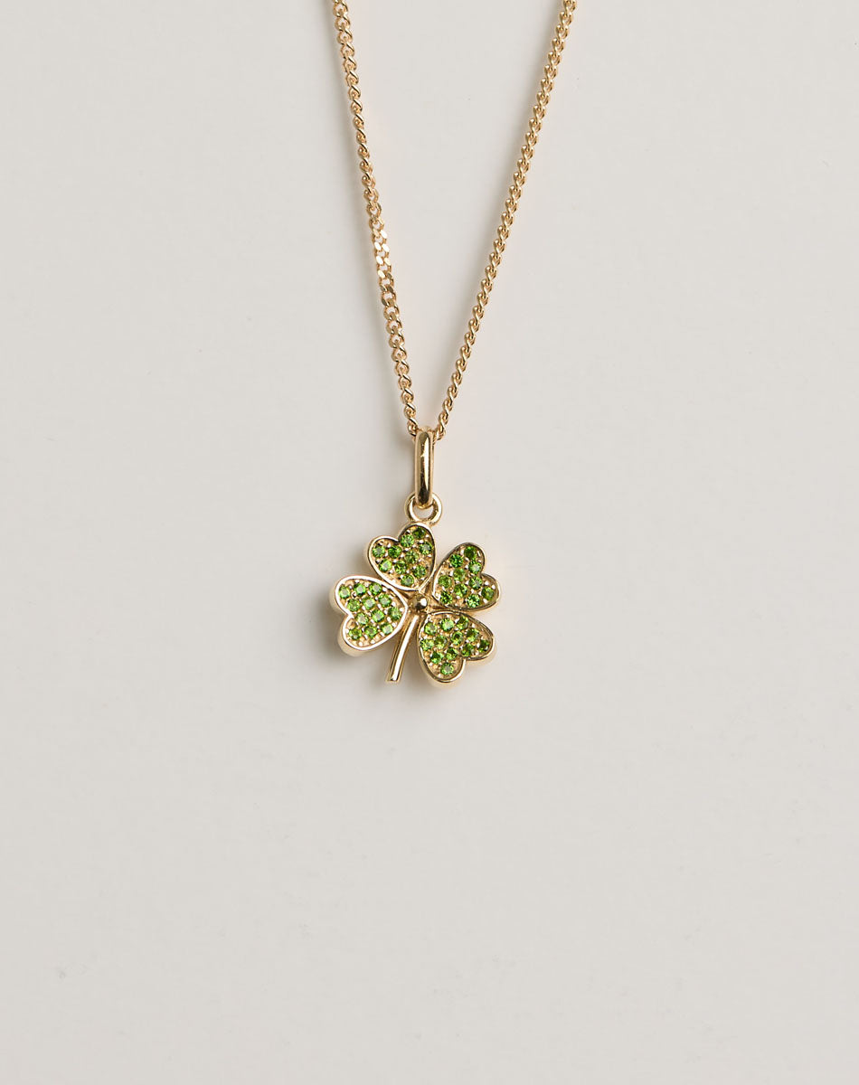 Gold necklace with a four-leaf clover pendant set with green gemstones on a light grey background