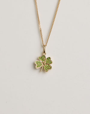 Gold necklace with a four-leaf clover pendant set with green gemstones on a light grey background