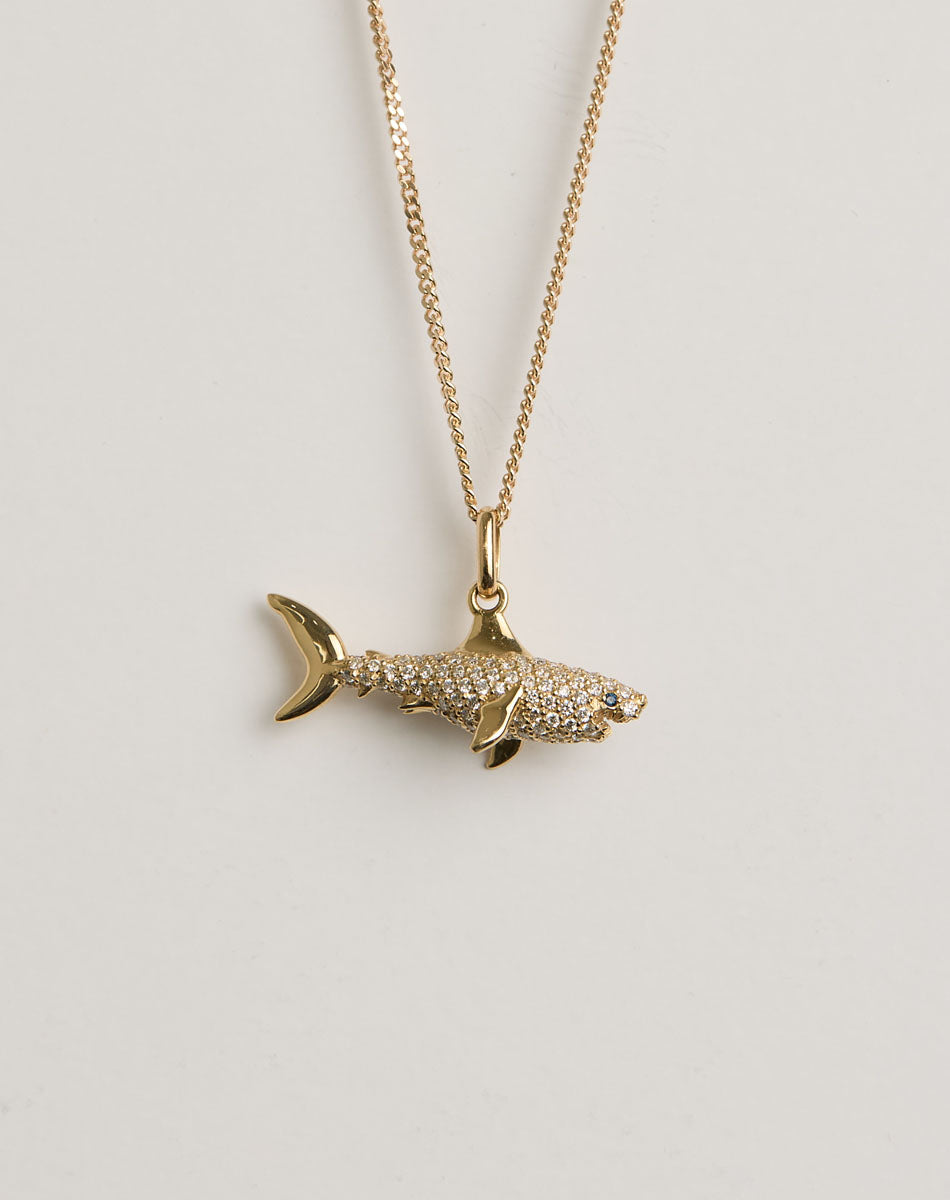 Gold and diamond shark pendant necklace on a light grey background