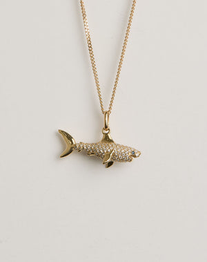 Gold and diamond shark pendant necklace on a light grey background