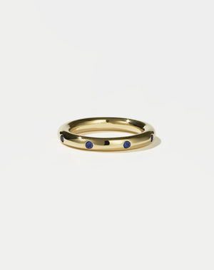 Gold ring with blue sapphires on a light gray background