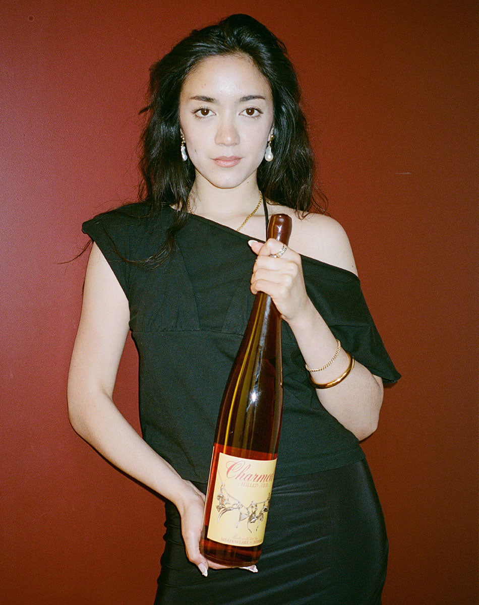 Woman holding a bottle of Charmed chilled red wine against a red background