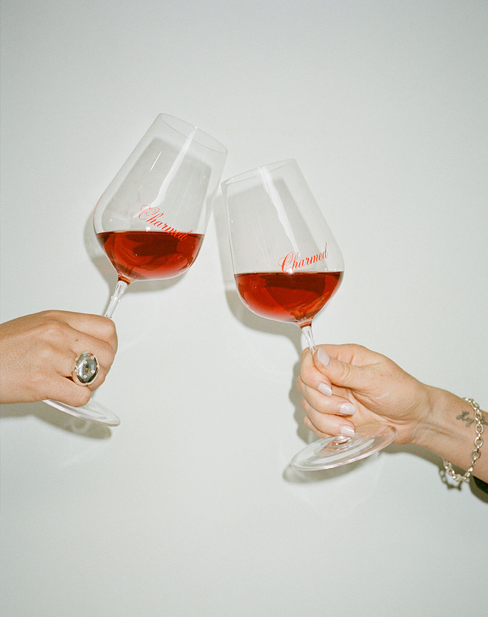 Two hands holding wine glasses with chilled red wine against a white background