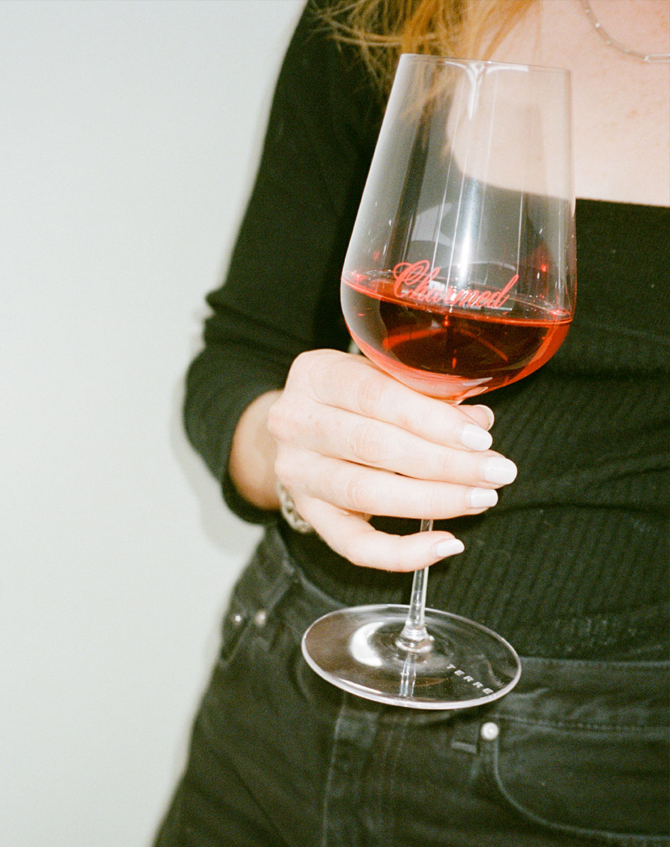 Person holding a glass of chilled red wine with 'Charmed' branding.