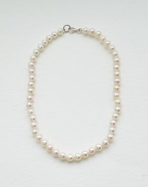 A freshwater pearl necklace with a classic round pearl design, strung on a silk thread and knotted.