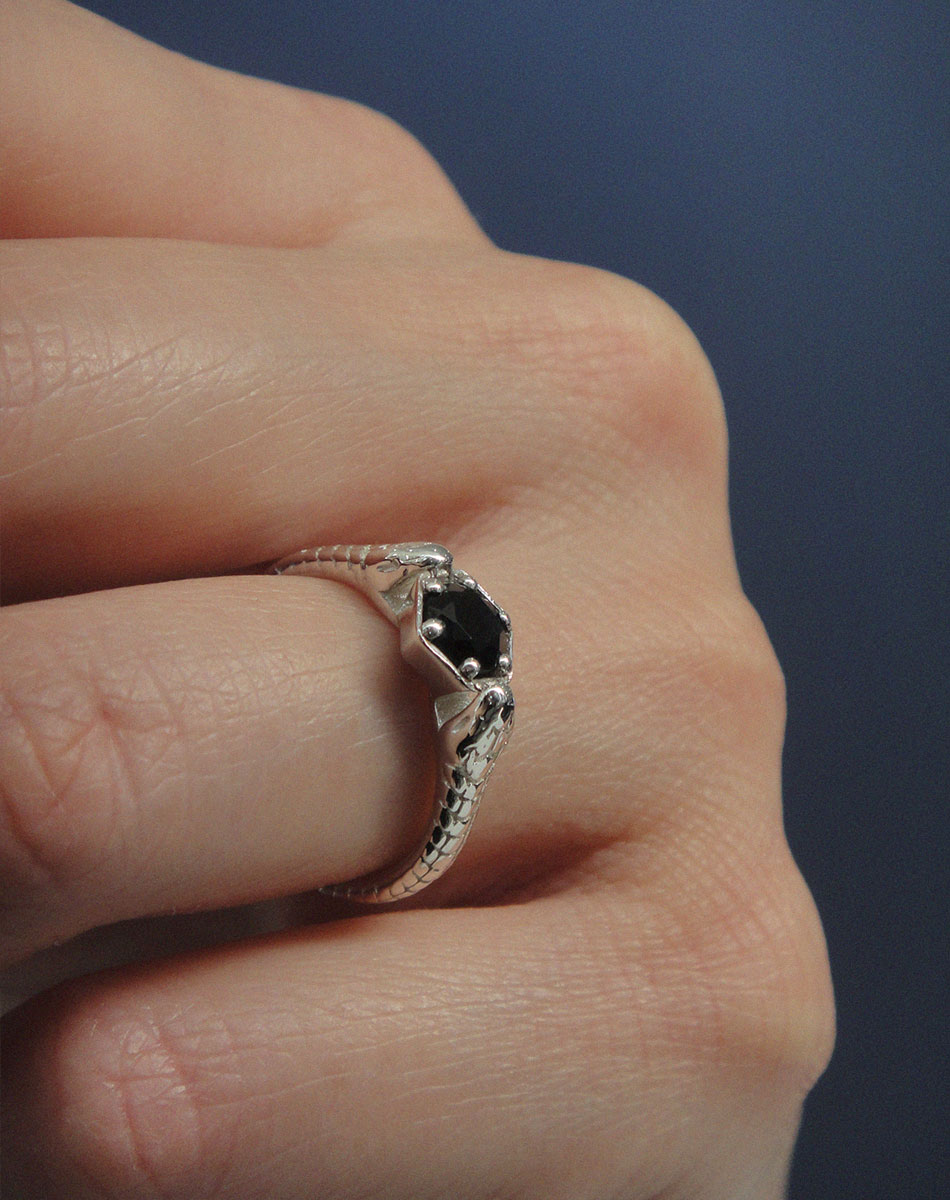Silver snake ring with a black gemstone on a hand against a dark background