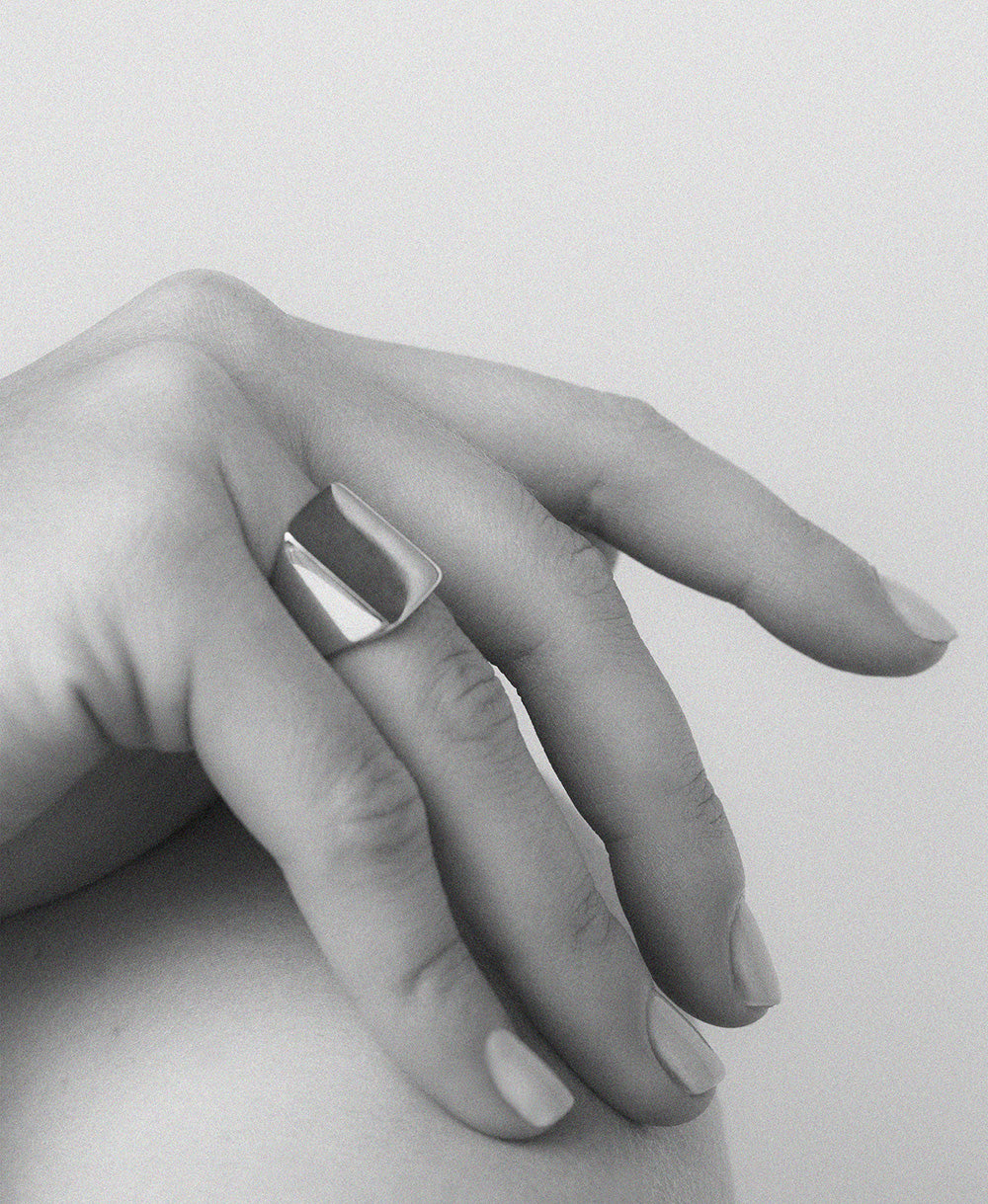 An oversized sterling silver signet ring with a flat rectangular platform for engraving, shown on a hand