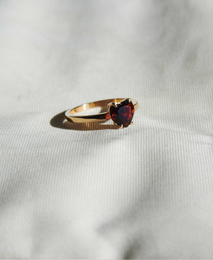A silver ring with a heart-shaped cut garnet stone set in a simple claw setting on a delicate band. Real life