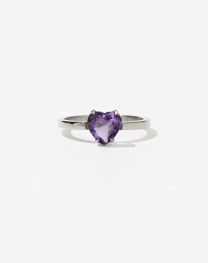 A silver ring with a heart-shaped cut amethyst stone set in a simple claw setting on a delicate band.