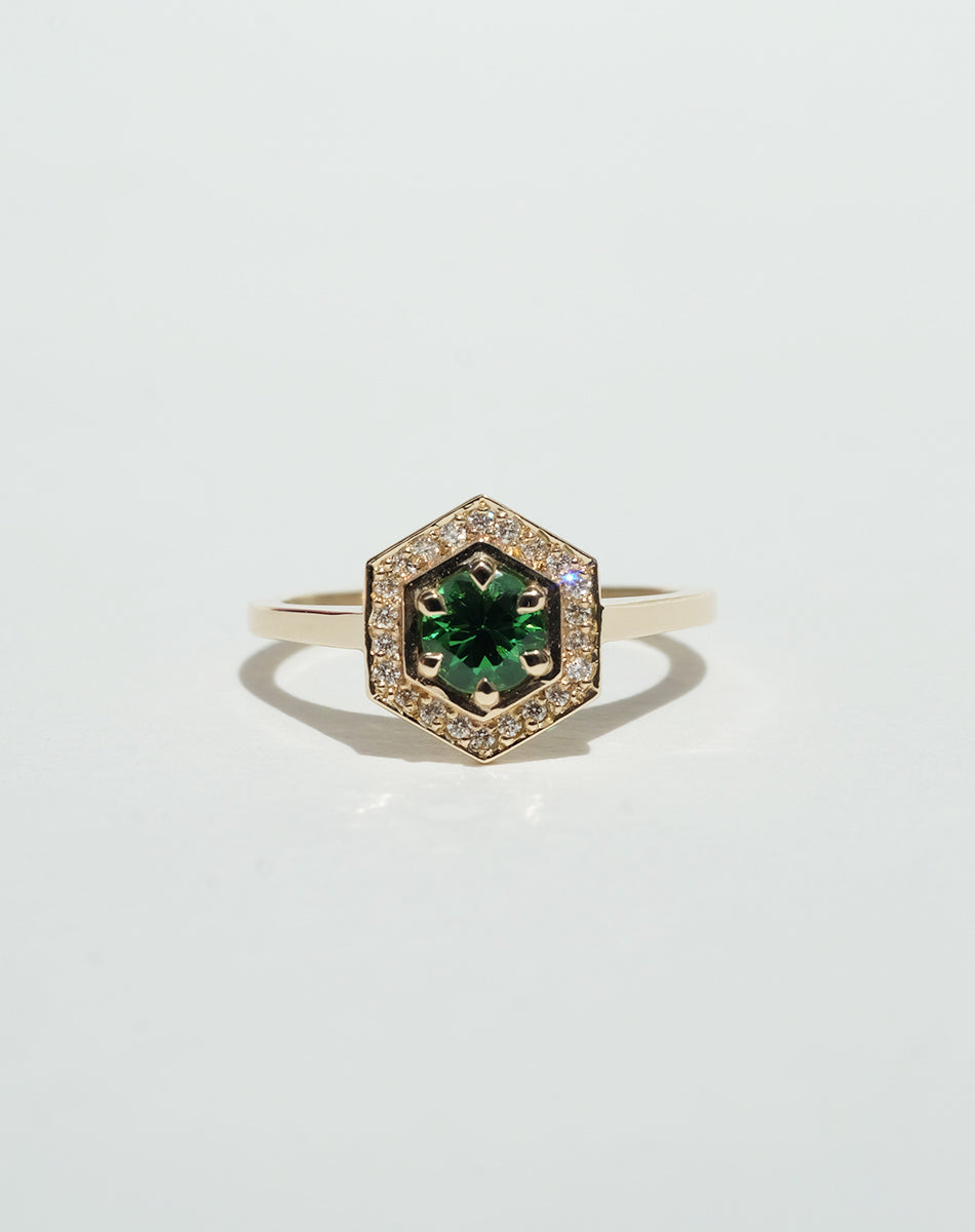 Meadowlark Jewellery’s Limited Edition Hex Engagement Ring 0.5ct in 9ct Yellow Gold, claw set with a round brilliant cut Tsavorite emerald Garnet centre stone, surrounded by a hexagon halo of pave set white diamonds. One of our most iconic and modern Ceremonial designs, made to order in New Zealand. Pair with our bestseller, the Diamond Eternity Band.
