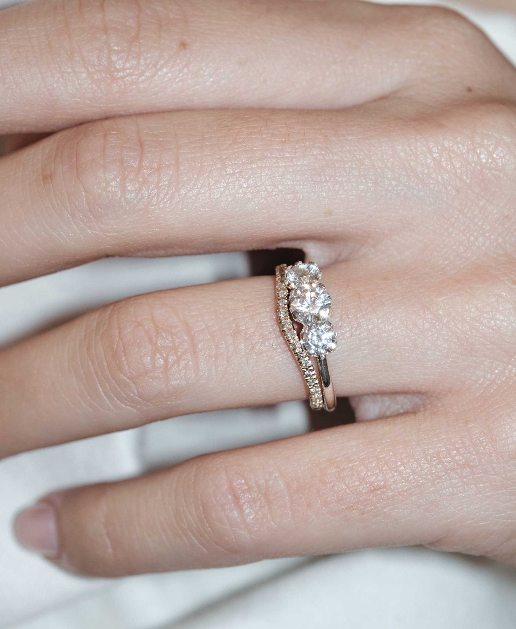 A classic three stone engagement ring in white gold with diamonds and a matching pave wedding band. On a hand.