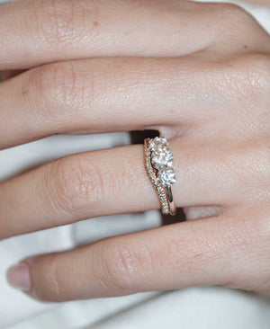 A classic three stone engagement ring in white gold with diamonds and a matching pave wedding band. On a hand.