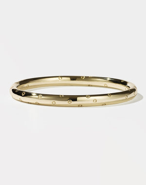 A gold-plated bracelet with small circles, likely representing strawberry seeds, spread out across the band.