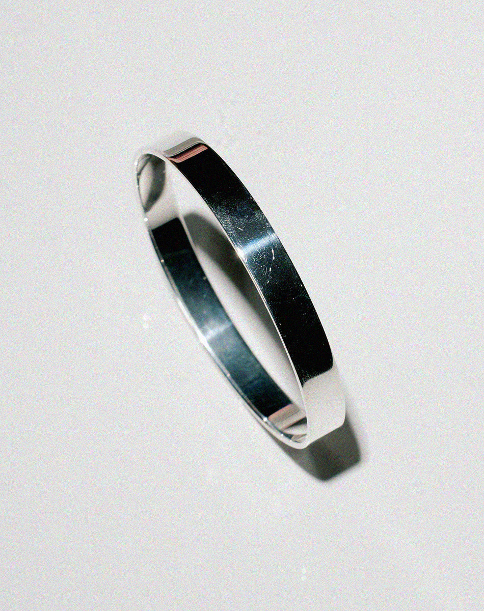 Side on view of a wide and flat sterling silver bangle.