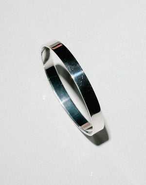 Side on view of a wide and flat sterling silver bangle.