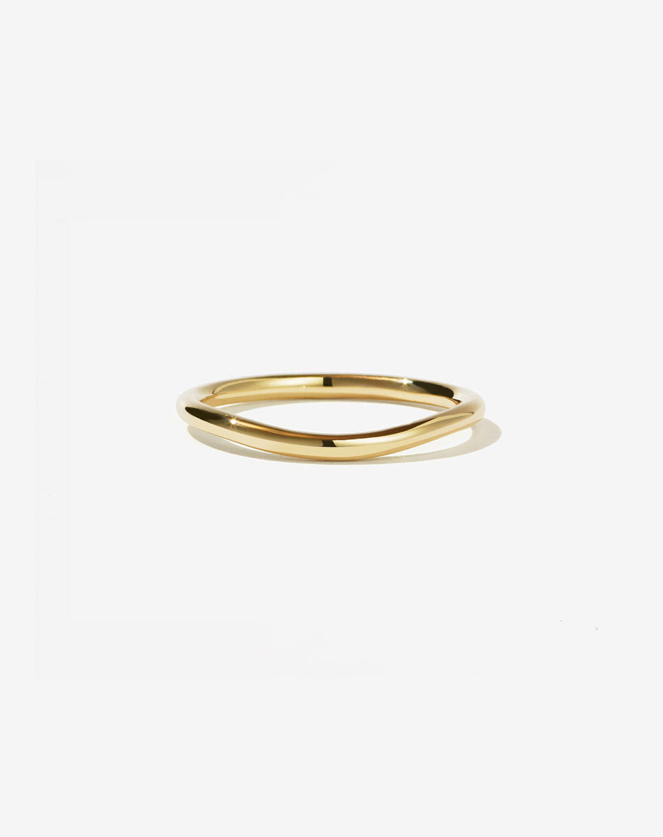 A simple gold band with a gentle curve, likely designed to be worn alongside an engagement ring.