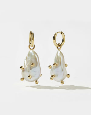A pair of gold drop earrings featuring baroque pearls with barnacle details.
