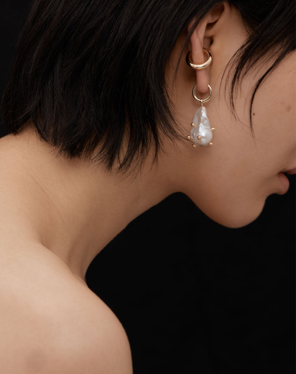 Woman wearing gold baroque pearl earrings with round dots like barnacles
