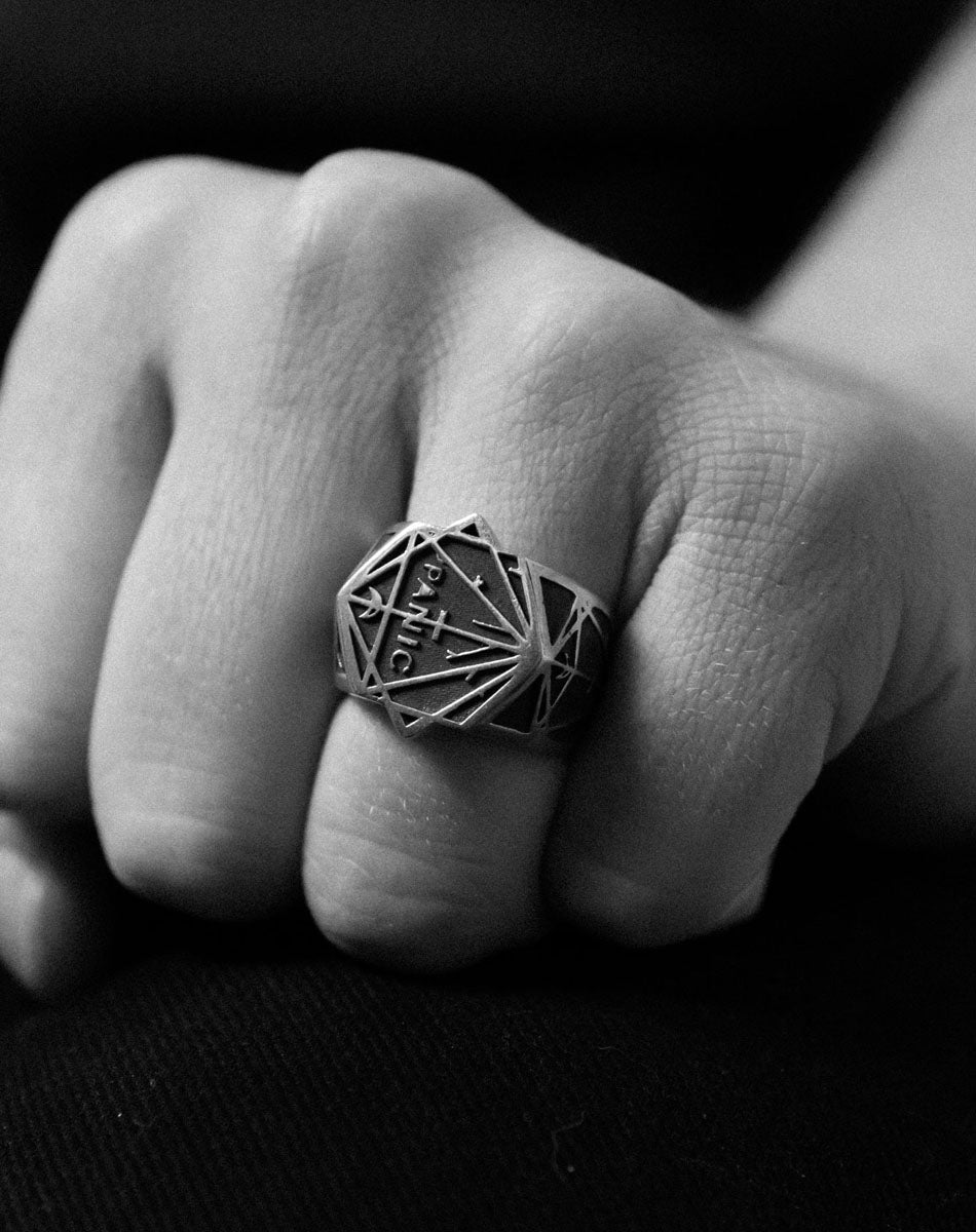 A heavy weighted sterling silver ring with a collage of black artworks designed by Andrew McLeod. Worn on a hand.
