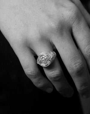 A sterling silver ring featuring a central artwork, collaged together, with intricate detailing. Worn on a hand