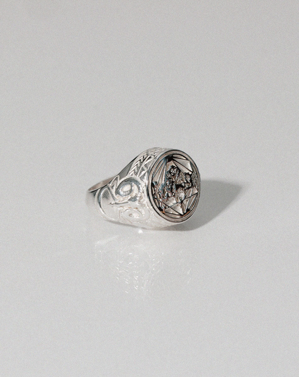 A sterling silver ring featuring a heavy weighted design with a central artwork, collaged together, with intricate detailing.