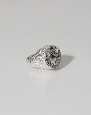 A sterling silver ring featuring a heavy weighted design with a central artwork, collaged together, with intricate detailing.