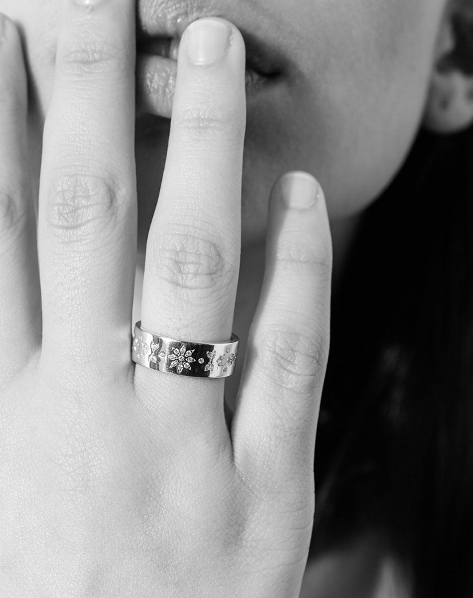 A 9 gold ring with ornate floral engravings set with diamonds and worn on a hand.