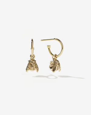 A pair of gold-colored hoop earrings with intricately-sculpted bee charms suspended from them.