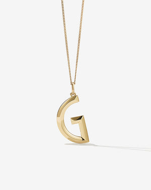 A gold pendant in the shape of a letter, with a faceted design.
