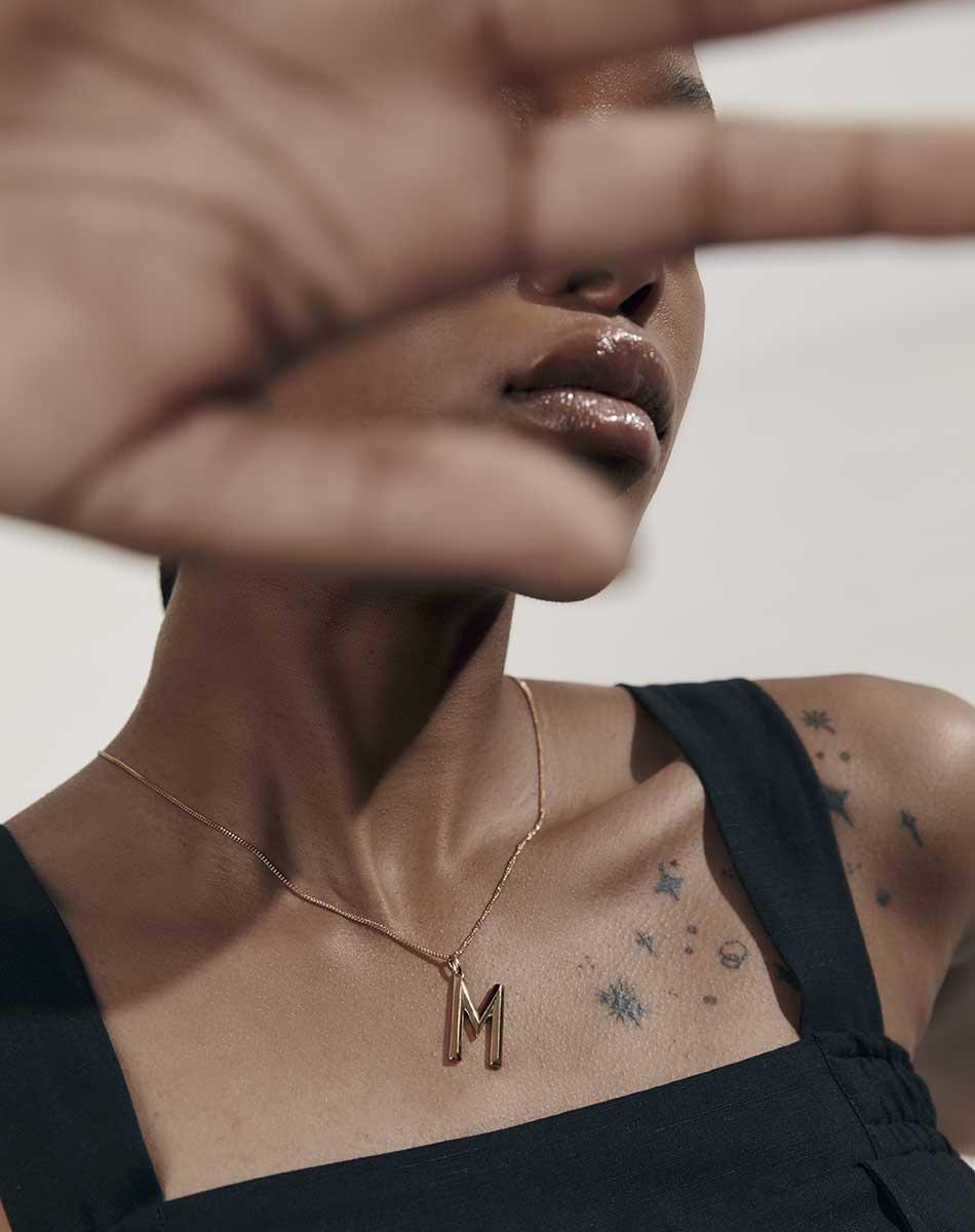 A gold pendant in the shape of a letter, with a faceted design. Shown on a model